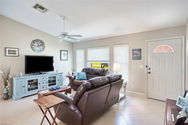 Living room with a ceiling fan, light tile patterned flooring, lofted ceiling, and visible vents