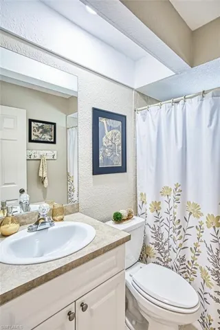 Bathroom featuring a textured wall, curtained shower, toilet, and vanity