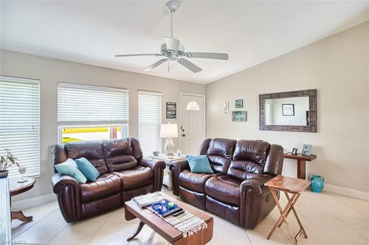 Living area with baseboards, a ceiling fan, vaulted ceiling, and light tile patterned floors