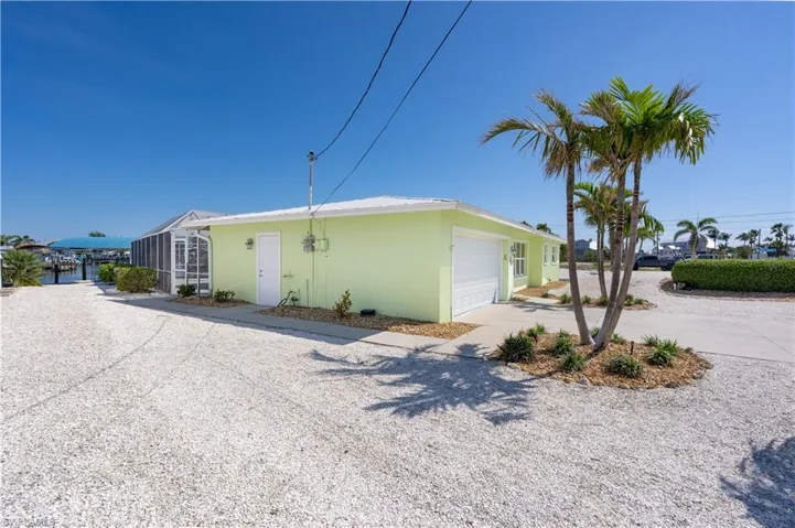 View of property exterior featuring driveway, stucco exterior, attached garage, and zero scaping with tropical flare