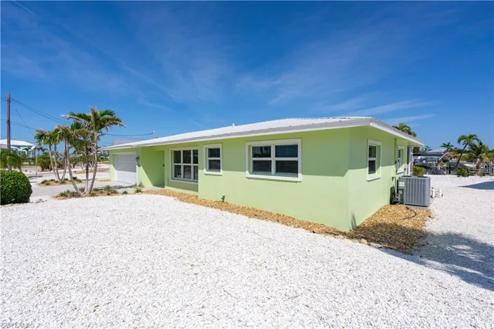 Rear view of property featuring gravel driveway, central AC, a garage, and stucco exterior.