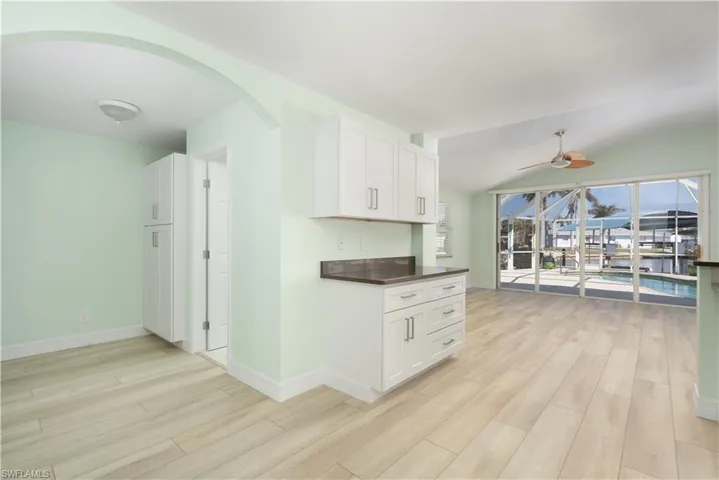Kitchen featuring white cabinets, arched walkways, ceiling fan, and light wood-style floors