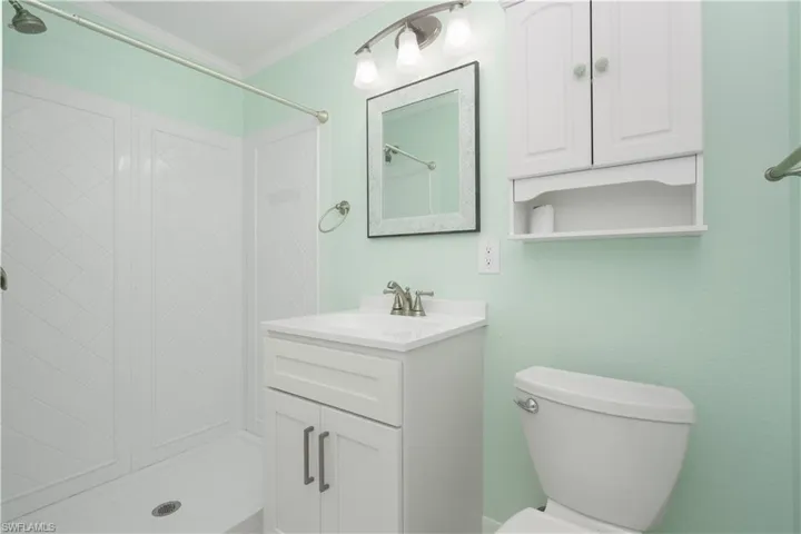 Bathroom featuring ornamental molding, walk in shower, toilet, and vanity.
