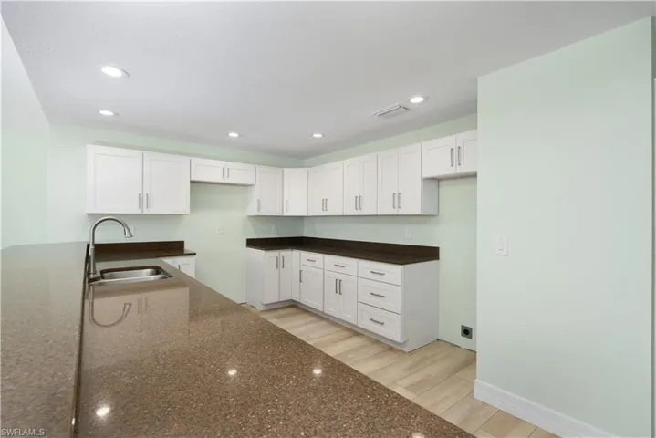 Kitchen featuring dark stone countertops, visible vents, white cabinetry, and a sink