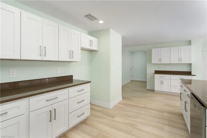 Kitchen with baseboards, arched walkways, light wood-type flooring, white cabinetry, and visible vents