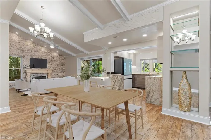 Dining area featuring vaulted ceiling with beams, light hardwood / wood-style flooring, a stone fireplace, and plenty of natural light