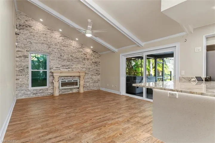 Unfurnished living room with a fireplace, lofted ceiling with beams, light hardwood / wood-style flooring, and ceiling fan