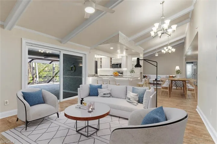 Living room with ceiling fan with notable chandelier, vaulted ceiling with beams, light wood-type flooring, and ornamental molding