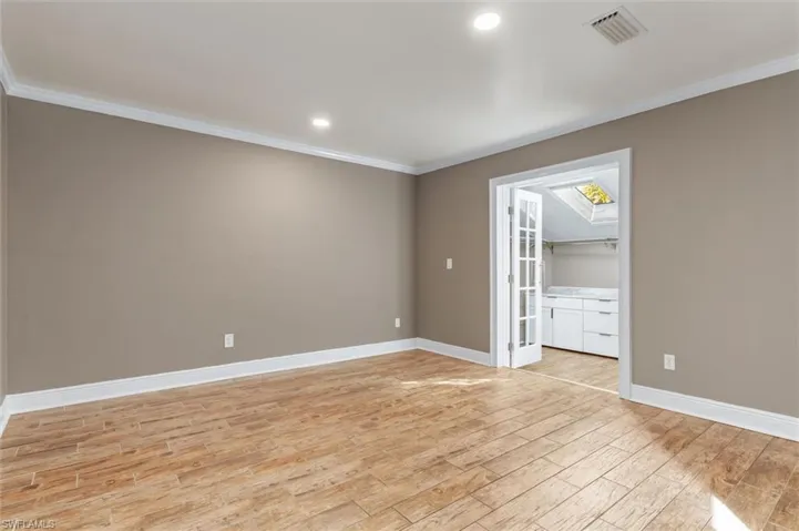 Unfurnished room with a skylight, light hardwood / wood-style flooring, and crown molding