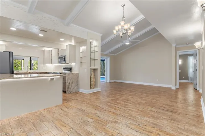 Unfurnished living room with sink, lofted ceiling with beams, crown molding, light hardwood / wood-style floors, and ceiling fan with notable chandelier