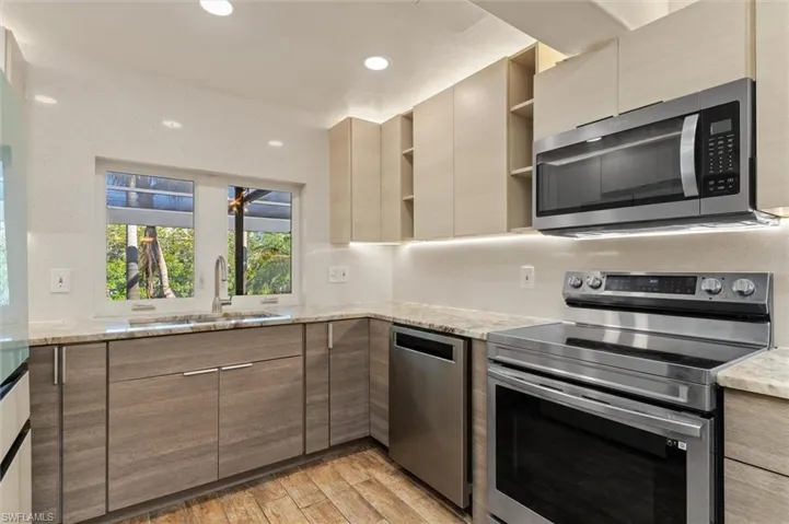Kitchen featuring light stone countertops, light wood-type flooring, stainless steel appliances, and sink