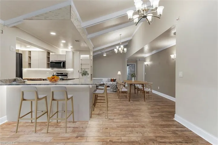 Kitchen with a kitchen breakfast bar, light hardwood / wood-style flooring, vaulted ceiling with beams, appliances with stainless steel finishes, and light stone counters