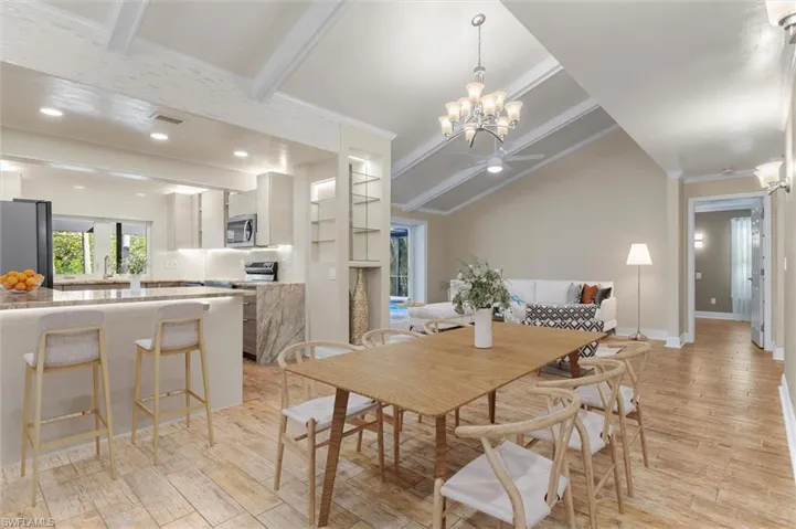 Dining space with ceiling fan with notable chandelier, sink, crown molding, vaulted ceiling with beams, and light wood-type flooring