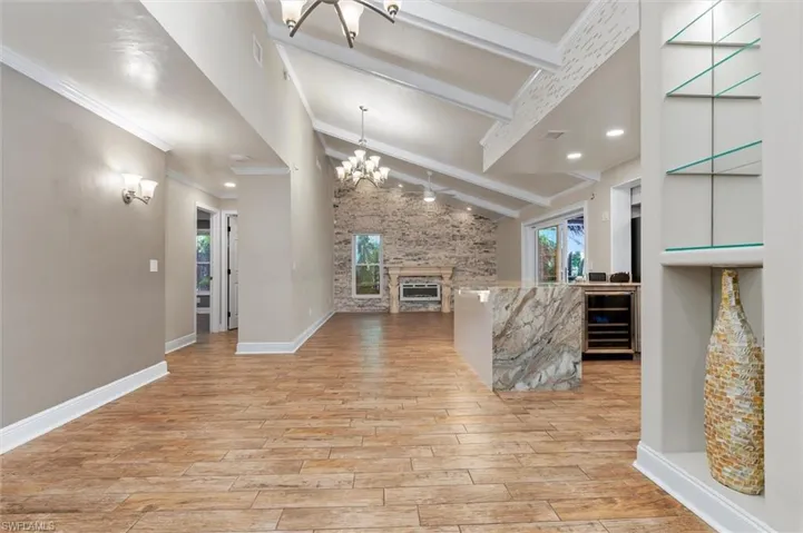 Unfurnished living room featuring wine cooler, light hardwood / wood-style floors, a stone fireplace, and ornamental molding