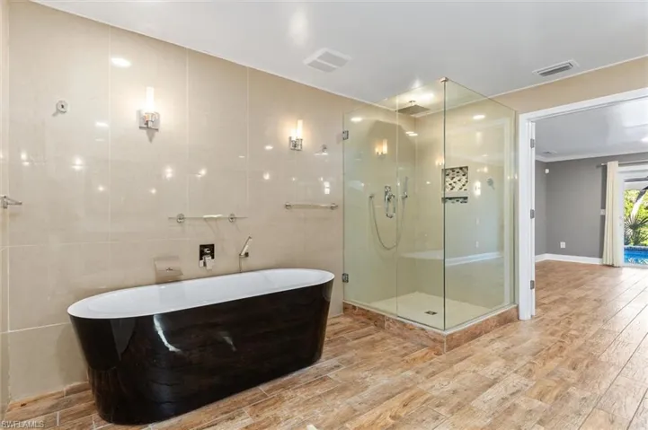 Bathroom featuring plus walk in shower, ornamental molding, tile walls, and hardwood / wood-style flooring