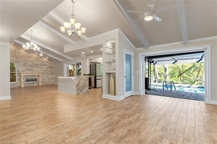 Unfurnished living room featuring vaulted ceiling with beams, a stone fireplace, crown molding, light hardwood / wood-style floors, and ceiling fan with notable chandelier