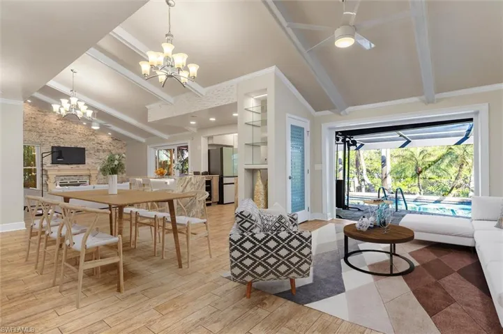 Dining room with a stone fireplace, lofted ceiling with beams, light wood-type flooring, ceiling fan with notable chandelier, and ornamental molding