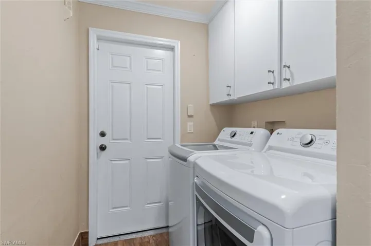 Washroom featuring dark hardwood / wood-style floors, cabinets, crown molding, and washing machine and clothes dryer