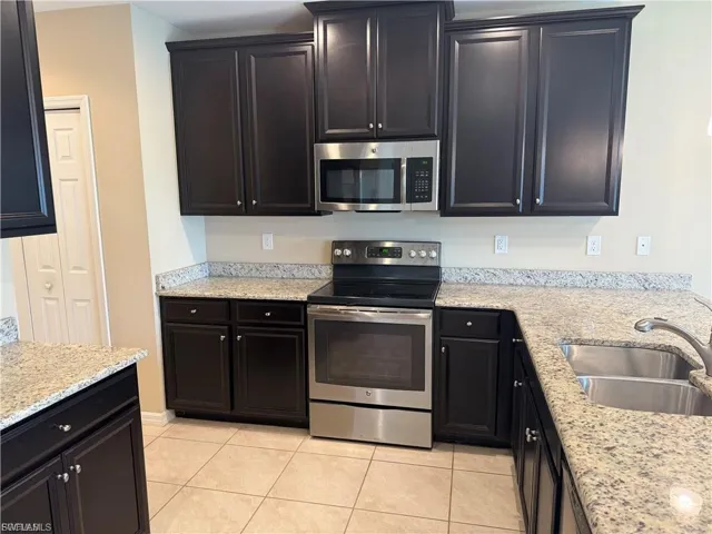Kitchen with stainless steel appliances, light stone counters, and light tile patterned floors