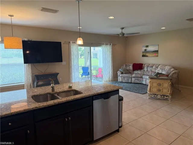 Kitchen featuring open floor plan, dark cabinets, stainless steel dishwasher, light stone countertops, and light tile patterned flooring