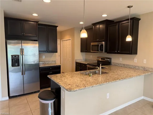 Kitchen featuring stainless steel appliances, light stone counters, light tile patterned floors, a peninsula, and dark wood finish cabinetry
