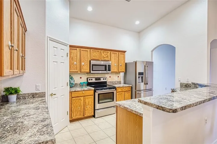 Kitchen featuring brown cabinetry, stainless steel appliances, backsplash, light tile patterned flooring, and arched walkways