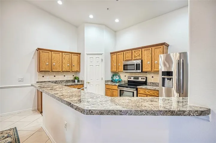 Kitchen featuring backsplash, brown cabinetry, appliances with stainless steel finishes, light tile patterned floors, and a towering ceiling