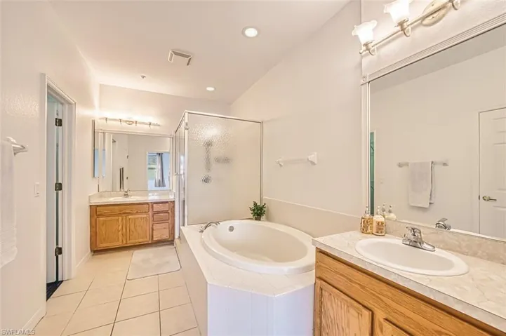 Full bathroom featuring a garden tub, two vanities, light tile patterned floors, a stall shower, and recessed lighting