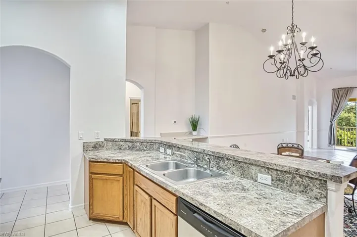 Kitchen featuring arched walkways, brown cabinets, decorative light fixtures, high vaulted ceiling, and light tile patterned floors