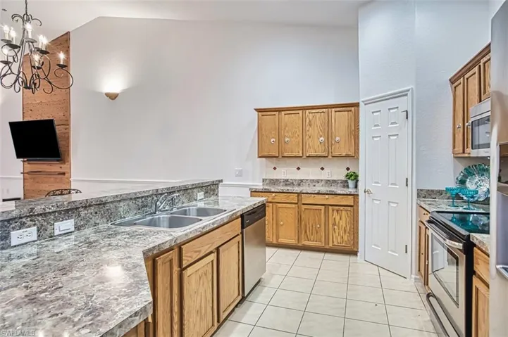 Kitchen with brown cabinetry, stainless steel appliances, light tile patterned floors, pendant lighting, and a chandelier