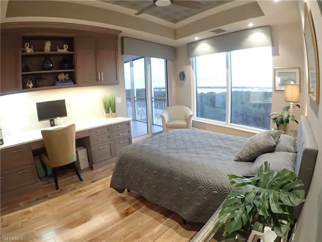 Bedroom featuring built in desk, access to exterior, a tray ceiling, light hardwood / wood-style flooring, and crown molding