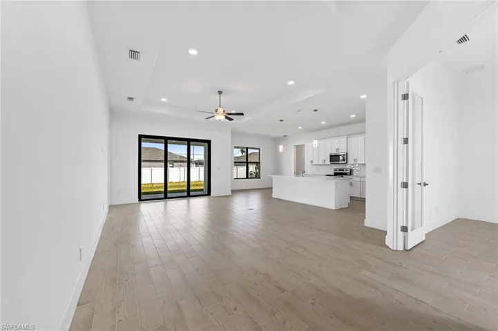 Unfurnished living room featuring ceiling fan, a raised ceiling, and light hardwood / wood-style flooring