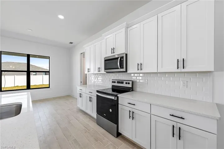 Kitchen with light stone counters, tasteful backsplash, light wood-type flooring, white cabinets, and appliances with stainless steel finishes