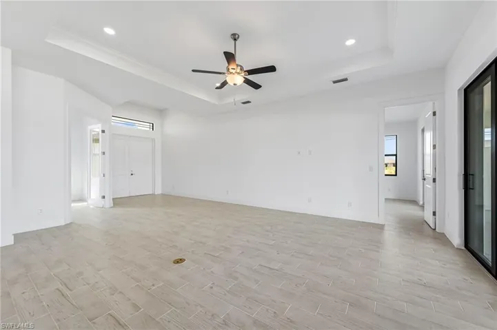 Empty room with ceiling fan, a tray ceiling, and light hardwood / wood-style flooring