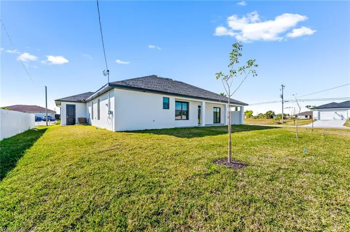 Back of house with central air condition unit, a garage, and a lawn