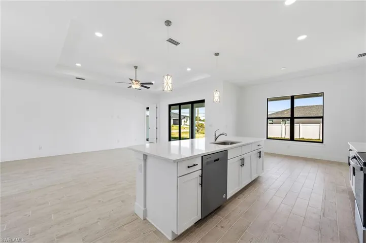 Kitchen featuring an island with sink, a tray ceiling, white cabinets, and appliances with stainless steel finishes