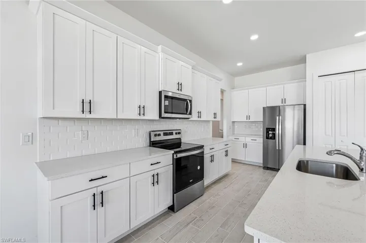 Kitchen featuring light stone counters, tasteful backsplash, white cabinetry, appliances with stainless steel finishes, and sink