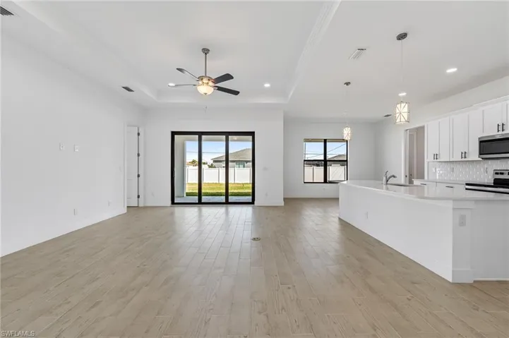 Kitchen featuring a tray ceiling, white cabinets, range with electric cooktop, pendant lighting, and tasteful backsplash