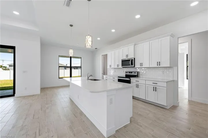 Kitchen featuring stainless steel appliances, white cabinetry, an island with sink, and plenty of natural light