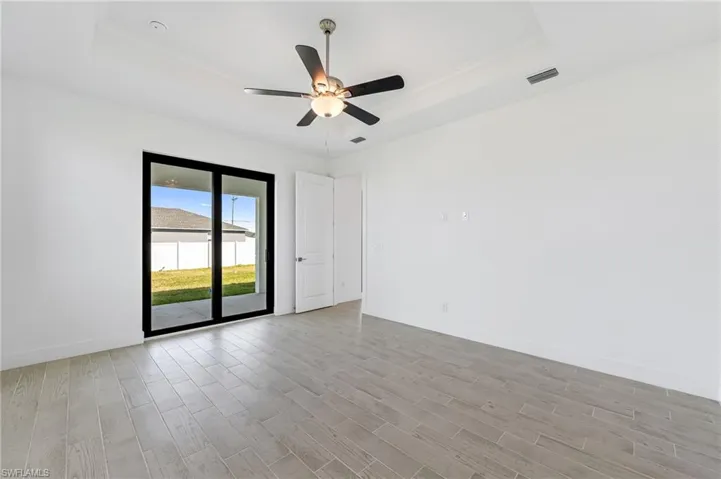 Unfurnished room with light wood-type flooring, ceiling fan, and a raised ceiling