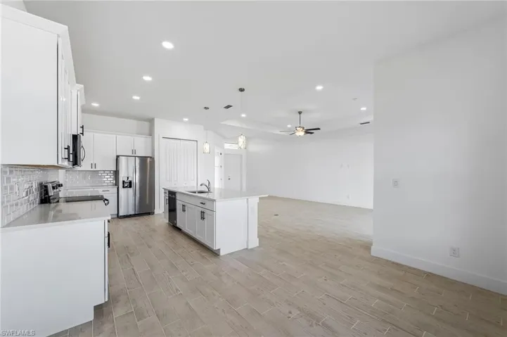 Kitchen featuring ceiling fan, tasteful backsplash, hanging light fixtures, a kitchen island with sink, and appliances with stainless steel finishes