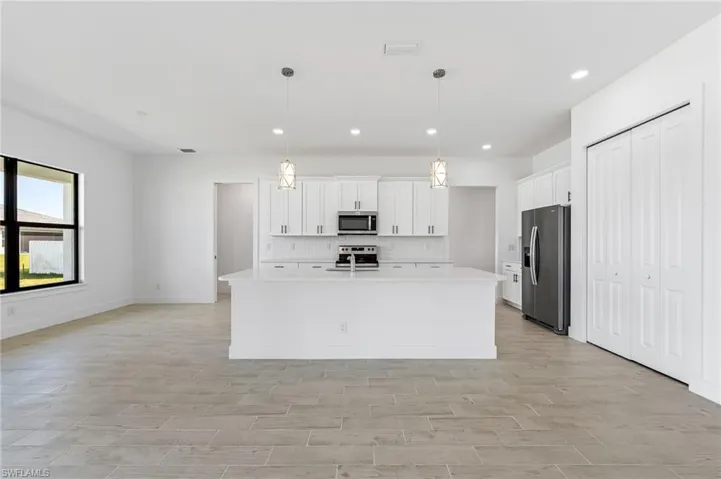 Kitchen featuring appliances with stainless steel finishes, an island with sink, tasteful backsplash, and pendant lighting