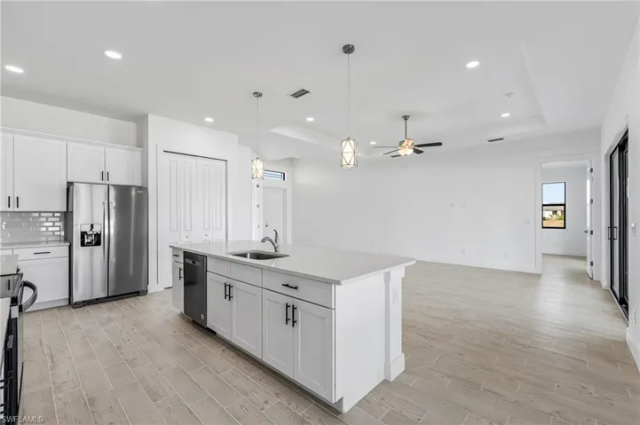 Kitchen featuring ceiling fan, a tray ceiling, a kitchen island with sink, and appliances with stainless steel finishes