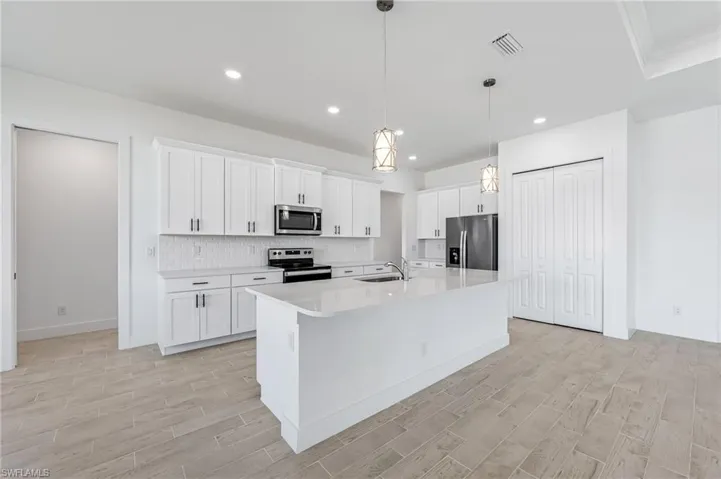 Kitchen with a center island with sink, appliances with stainless steel finishes, white cabinets, pendant lighting, and sink