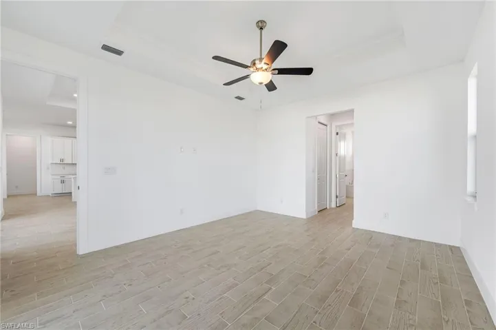 Spare room with ceiling fan, a raised ceiling, and light wood-type flooring