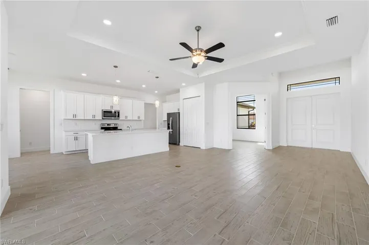 Kitchen with an island with sink, ceiling fan, a tray ceiling, and appliances with stainless steel finishes