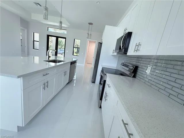 Kitchen with white cabinetry, light stone counters, stainless steel appliances, and hanging light fixtures