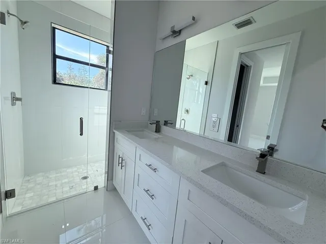 Bathroom with a shower stall, double vanity, and light tile patterned flooring