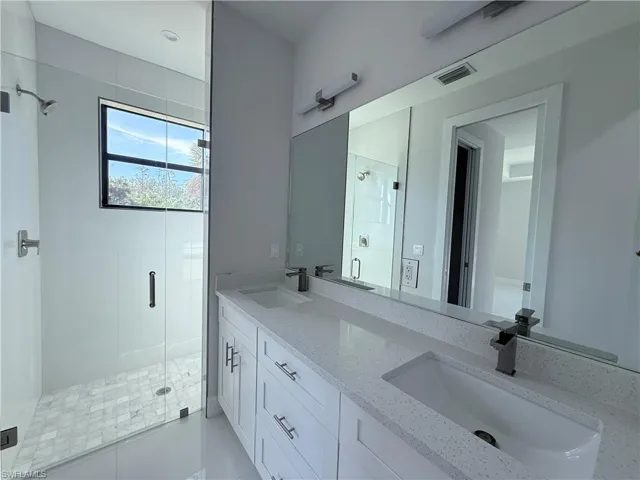Bathroom featuring double vanity, a stall shower, and light tile patterned flooring