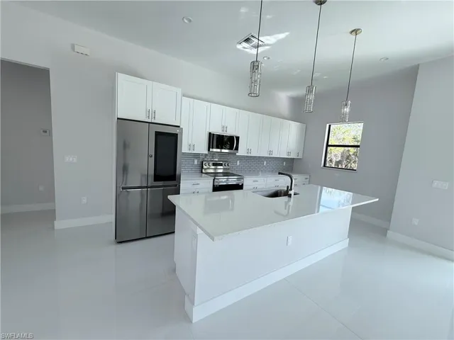 Kitchen featuring stainless steel appliances, white cabinetry, light tile patterned floors, and light stone counters